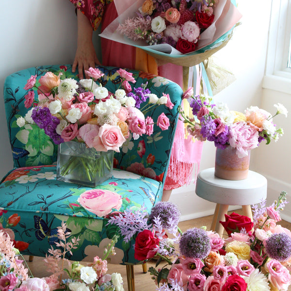 A mass of flowers arranged in various vases are placed around a chair and side table.