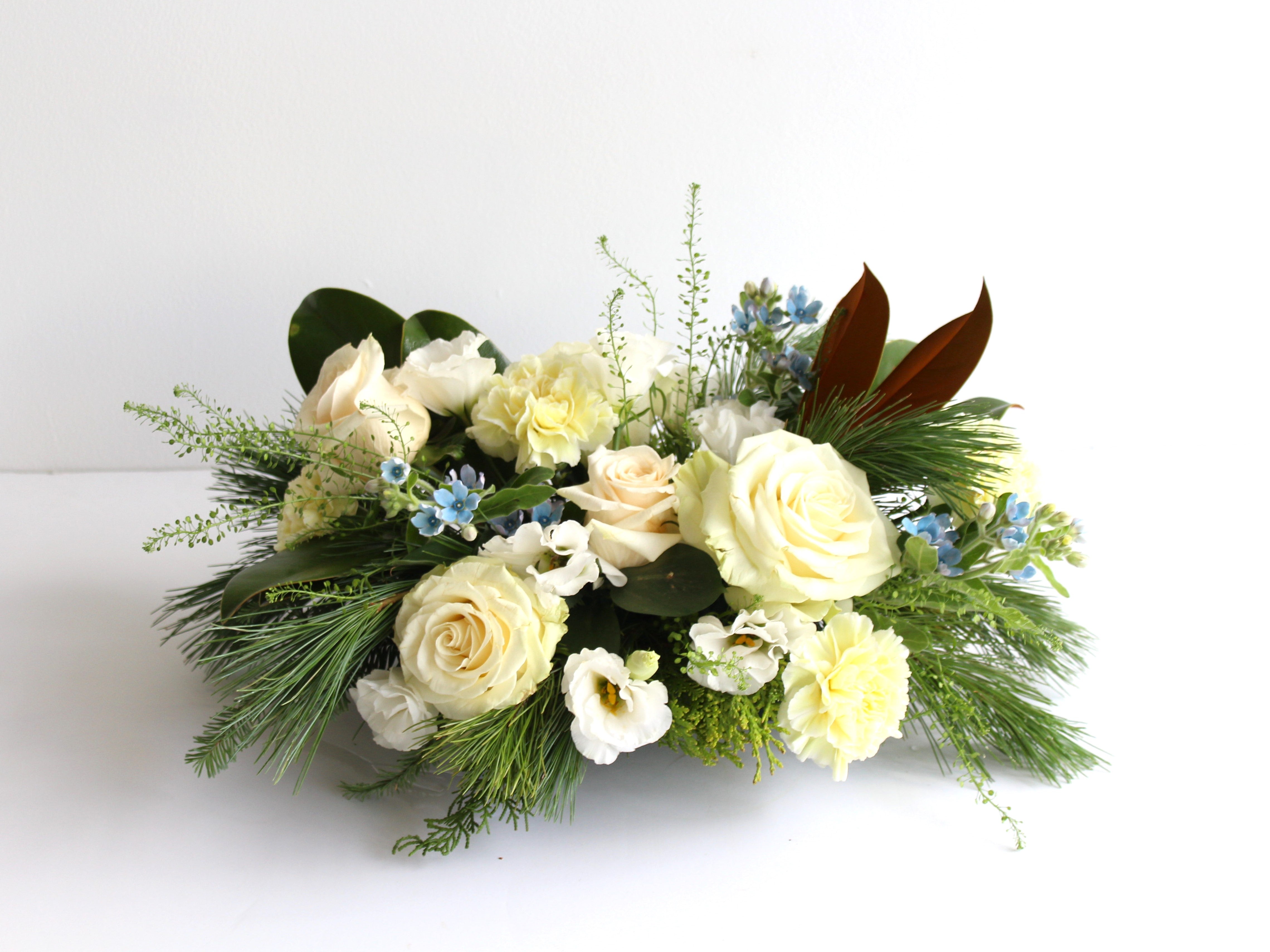 A low arrangement of white flowers with some pale blue accent flowers.