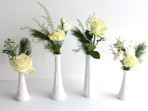 Four white milkglass budvases lined up against a white background. each vase has a cluster of flowers.