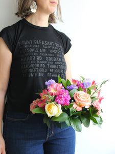 Toronto florist Periwinkle Flowers is holding a small low floral centerpiece, standing in front of a white wall.