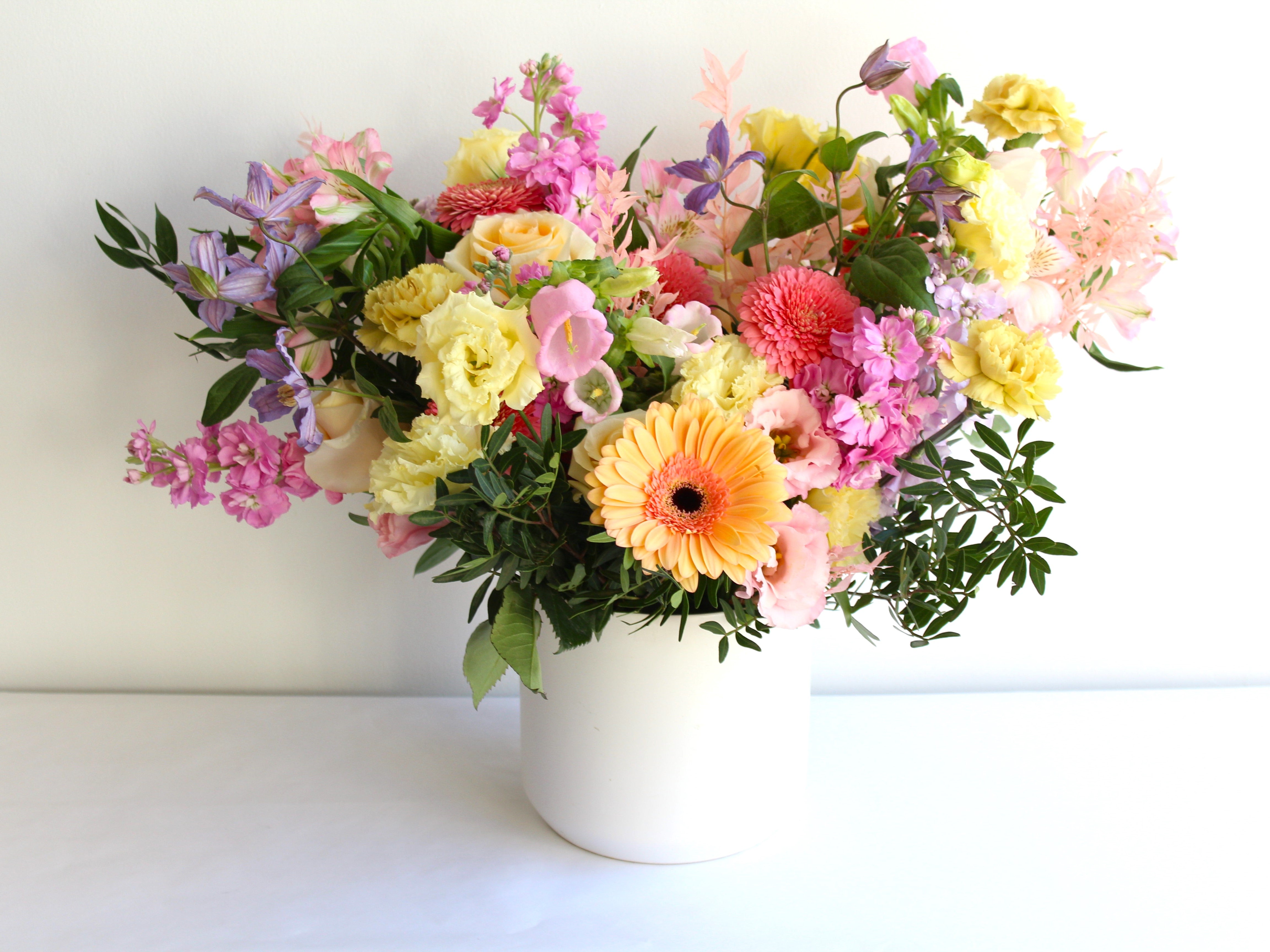 A white ceramic pot is filled with pastel flowers and set  against a white background.