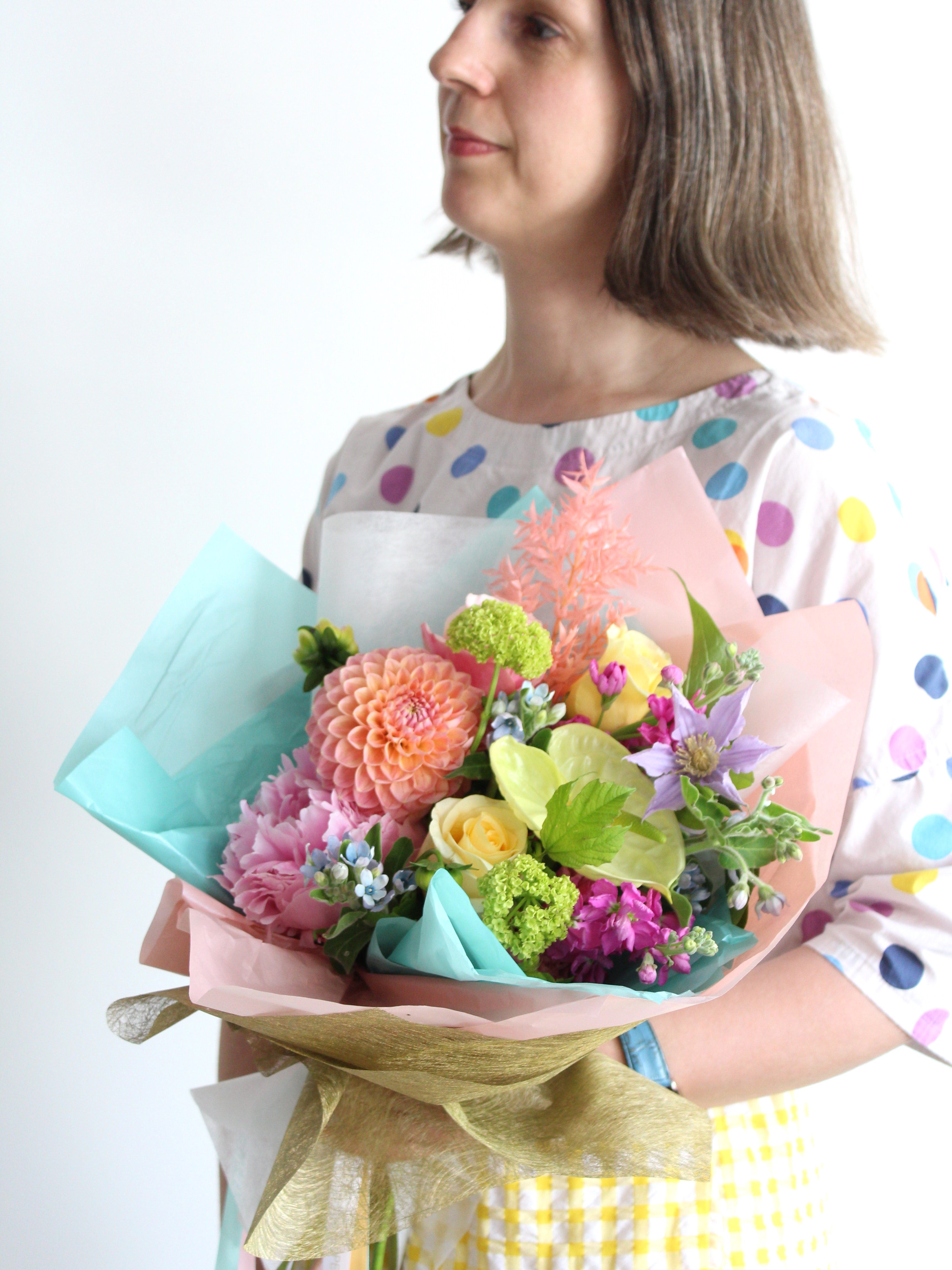 A pastel toned seasonal and unique flower bouquet wrapped in colourful tissue is held by florist Periwinkle Flowers, ready for delivery in Toronto.