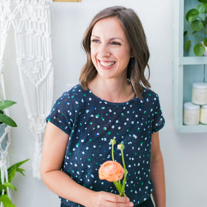 Toronto florist Jess McEwen of Periwinkle Flowers is standing in her studio holding a peach ranunculus.