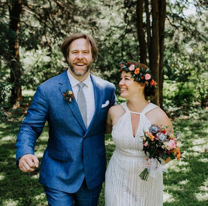 A bride and groom holding colourful wedding bouquet walk in the woods in a Toronto park.